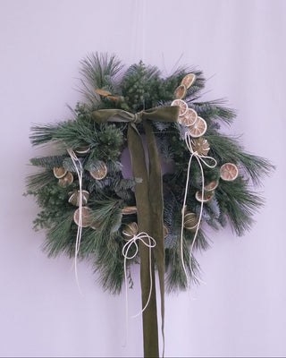 Decorative christmas wreath with greenery, ribbons, and citrus slices on a white background